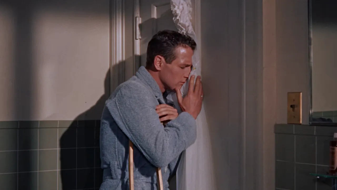 Brick Pollitt (Paul Newman), in a bathrobe and leaning on a crutch, presses his face into a ruffled shower curtain in the bathroom.