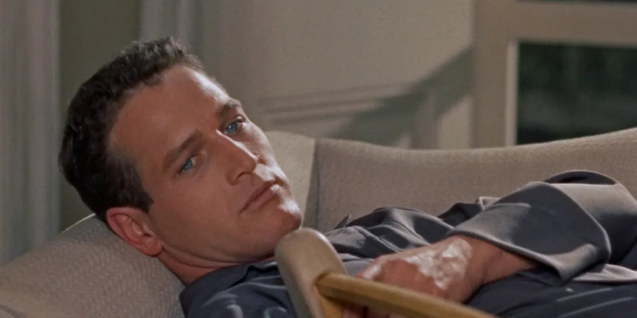Brick Pollitt (Paul Newman) lies on a sofa holding a wooden crutch across his chest, looking away with a closed-off expression.